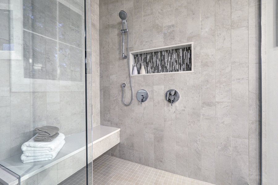 Glass walk-in shower with gray subway tiled surround accented with mosaic tile strip in wall niche of brand new home bathroom. Northwest USA