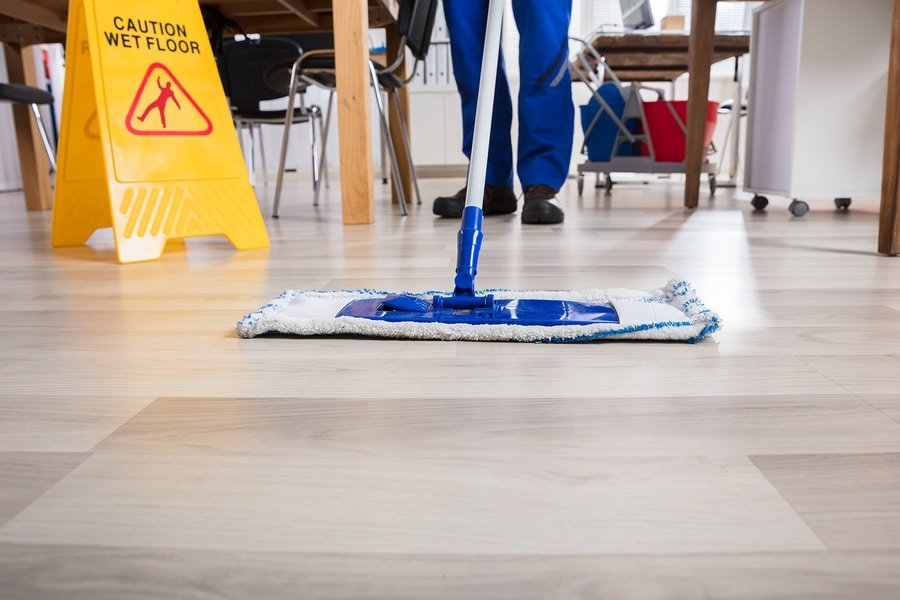 Janitor Cleaning Floor In Front Of Yellow Caution Wet Floor Sign