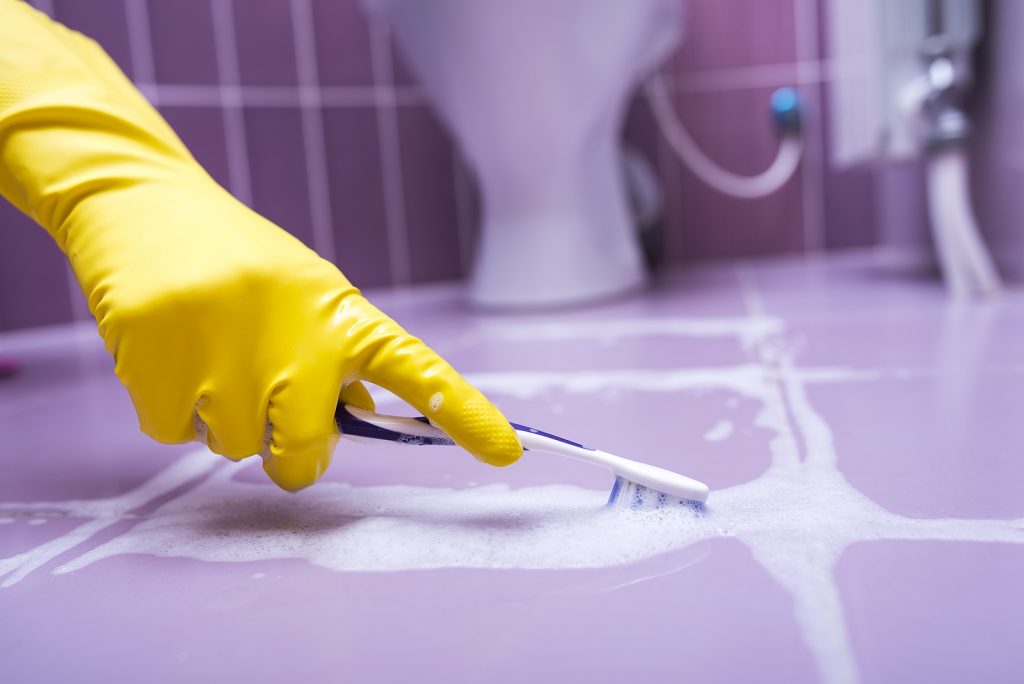 Hand in yellow glove cleans the tile toothbrush.