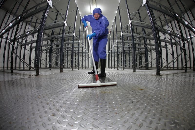 worker in protective uniform cleaning floor in empty warehouse