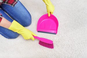 Female hands in yellow gloves sweeping a carpet brush.